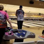 Bowling alley scene with a bowler and lane equipment under overhead scoreboards.