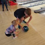 Child and adult playing mini golf indoors on a wooden court.