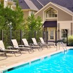 Poolside loungers in front of a modern, upscale residential building with lush greenery.