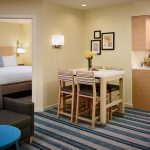 Modern hotel room with dining area, comfortable seating, and view into a bedroom.