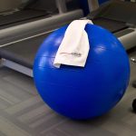 Blue exercise ball with white towel on gym floor near treadmills.