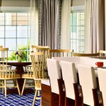 Modern dining area with wooden chairs, large windows, and a white table setting.