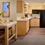 Modern kitchen with light wood cabinets, white countertops, and a breakfast bar area.