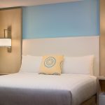 Modern hotel room with a large bed, blue accent wall, and contemporary bedside lighting.