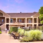Two-story apartment building with balconies and outdoor patio area under a clear sky.