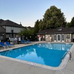 Outdoor swimming pool area with surrounding concrete deck and apartment buildings under a clear sky.