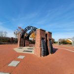 Brick archway entrance with black metalwork under a bright blue sky.