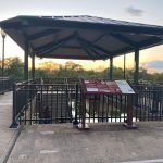 Pavilion overlooking a waterway at sunset with informational display board.