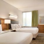 Bright hotel room with two comfortable beds, modern decor, and large window.