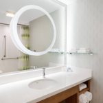 Modern bathroom vanity with large circular mirror, white countertop, and shelves.