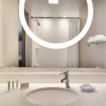 Modern bathroom vanity with large circular mirror, sink, and white countertop.