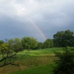 Rainbow over a green golf course under dramatic, cloudy skies.