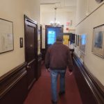Man walks down a long, carpeted hallway in an institutional building.