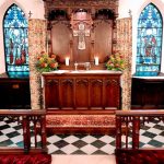 Ornate wooden reredos and altar in a Gothic church interior with stained glass windows.