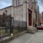 Historic brick church facade with black iron fence on a cloudy city street.