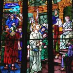 Stained glass panel depicting biblical scene with multiple figures in historical attire.