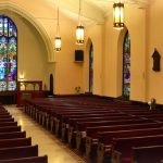 Interior view of a church sanctuary with wooden pews and stained glass windows.