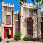Historic, imposing stone building with Gothic-style arched windows under a bright blue sky.