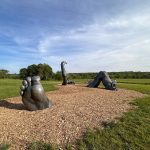 Sculptures of a giant foot, serpent, and archway in an open grassy field under a blue sky.
