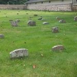 Ancient stone markers scattered across a grassy field near a historic building.