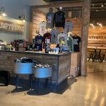 Retail shop interior featuring a wooden counter, merchandise racks with t-shirts, and industrial decor.
