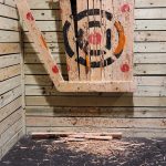 Handcrafted wooden block with painted circular design mounted on rustic wood paneling.