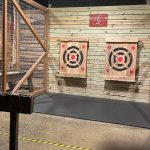 Indoor axe throwing range with wooden targets mounted on a slatted wall.