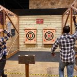 Two men practice shooting at targets inside a wooden indoor archery range.