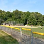 Outdoor sports field with trees lining the background under a clear blue sky.