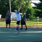 Basketball players practice outdoors on a court under sunny skies.