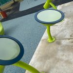 Bright green outdoor exercise equipment with circular platforms on a paved area.