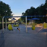 Outdoor fitness park with equipment and people exercising under a clear blue sky.