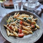 Pasta dish with shrimp and vegetables served on a speckled plate at a restaurant table.