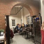 Brick archway entrance to a modern bar area with patrons and wine racks.