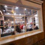 Restaurant interior view through a large window, showing diners and cafe ambiance.