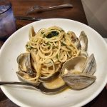 Pasta with clams served in a white bowl on a dark wooden table.
