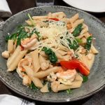 Pasta with shrimp, spinach, and cheese in a rustic grey bowl.
