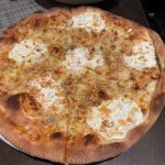 Golden-brown, rustic pizza with cheese and visible toppings on a dark surface.