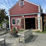 Red barn with large open bay doors, gravel driveway, and flower pots.