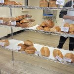Bakery shelves stocked with various breads and rolls, with a person serving customers.