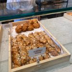 Assortment of almond croissants and sticks displayed in a wooden tray at a bakery counter.