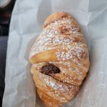 Almond croissant dusted with powdered sugar on white parchment paper.