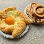 Pastry with egg yolk and cinnamon roll on wooden surface.