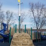 Children's playground with blue slide and climbing structure under bare trees.