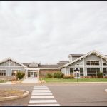 Modern, light gray clubhouse with large windows under a cloudy sky.