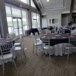 Large indoor event space with high ceilings, windows, and set tables for a gathering.