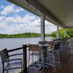 Outdoor deck with dining area overlooking a calm lake under a partly cloudy sky.