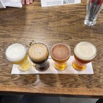 Four glasses of beer on a wooden table with a Google QR code in the background.