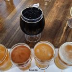 Assortment of craft beers, including dark stout and various light ales, on a wooden table.