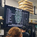 Bar display showing beer taps menu next to stacked bags of brewing ingredients.